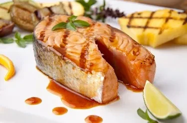 Orange-pink grilled salmon with grill marks, sauce, lime, and blurred sides.