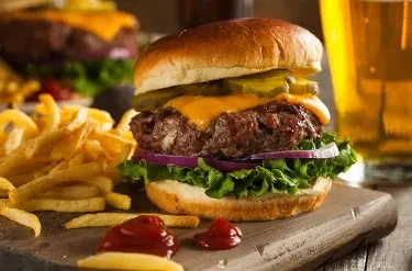 Classic cheeseburger, golden french fries, and ketchup on a wooden board.