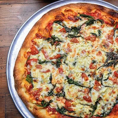 Pizza with melted cheese, tomatoes, spinach, and herbs on a silver pan.