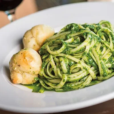 Green pasta with bread rolls and a glass of red wine.
