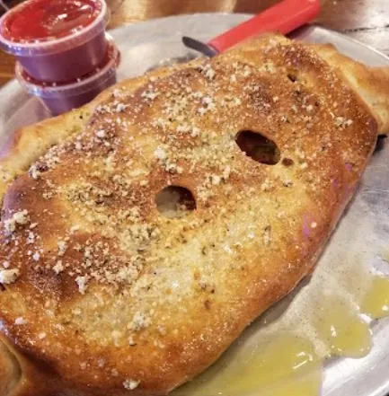 Large golden-brown calzone topped with Parmesan and herbs on a metal tray.