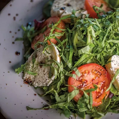 Close-up, overhead salad with arugula, tomatoes, mozzarella, black pepper, balsamic.