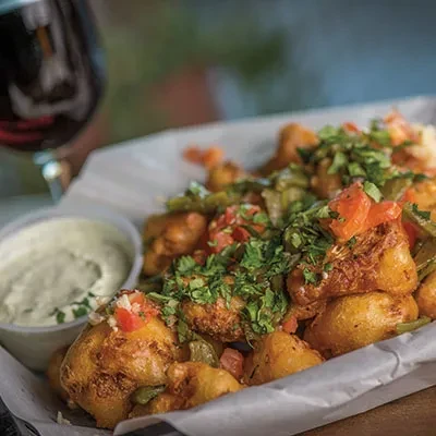 Crispy fried vegetables topped with herbs, tomatoes, and dipping sauce.
