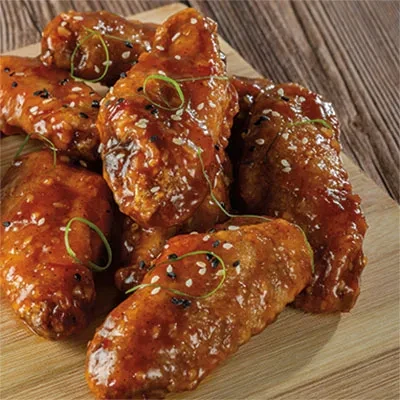 Glazed chicken wings with sesame seeds and green onions on a wooden board.
