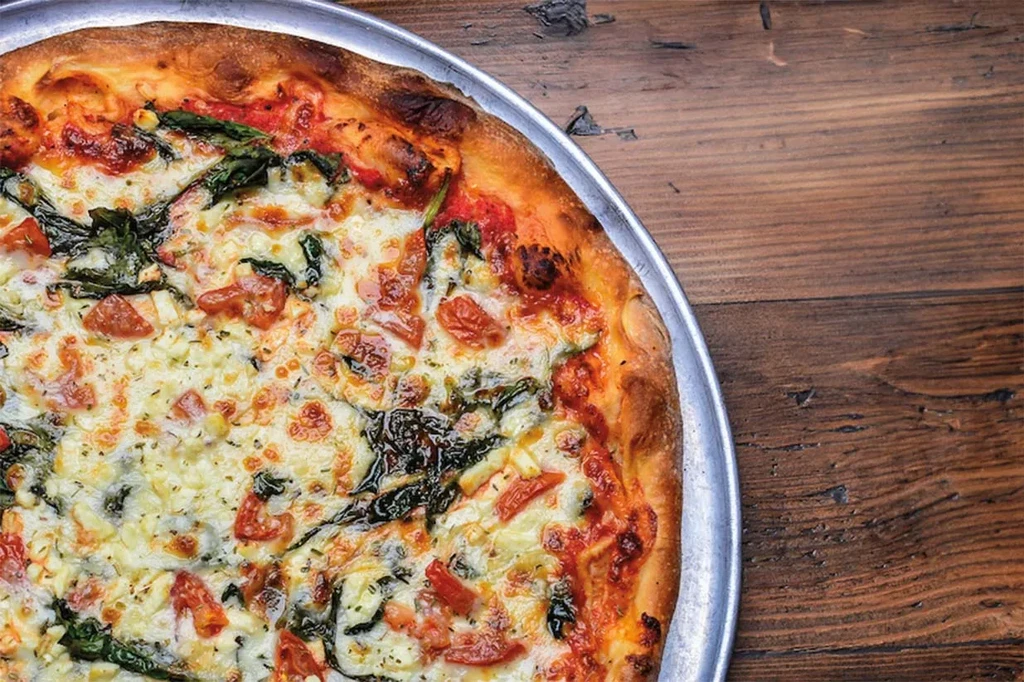 Freshly baked pizza with tomato, mozzarella, spinach, and herbs on a pan.