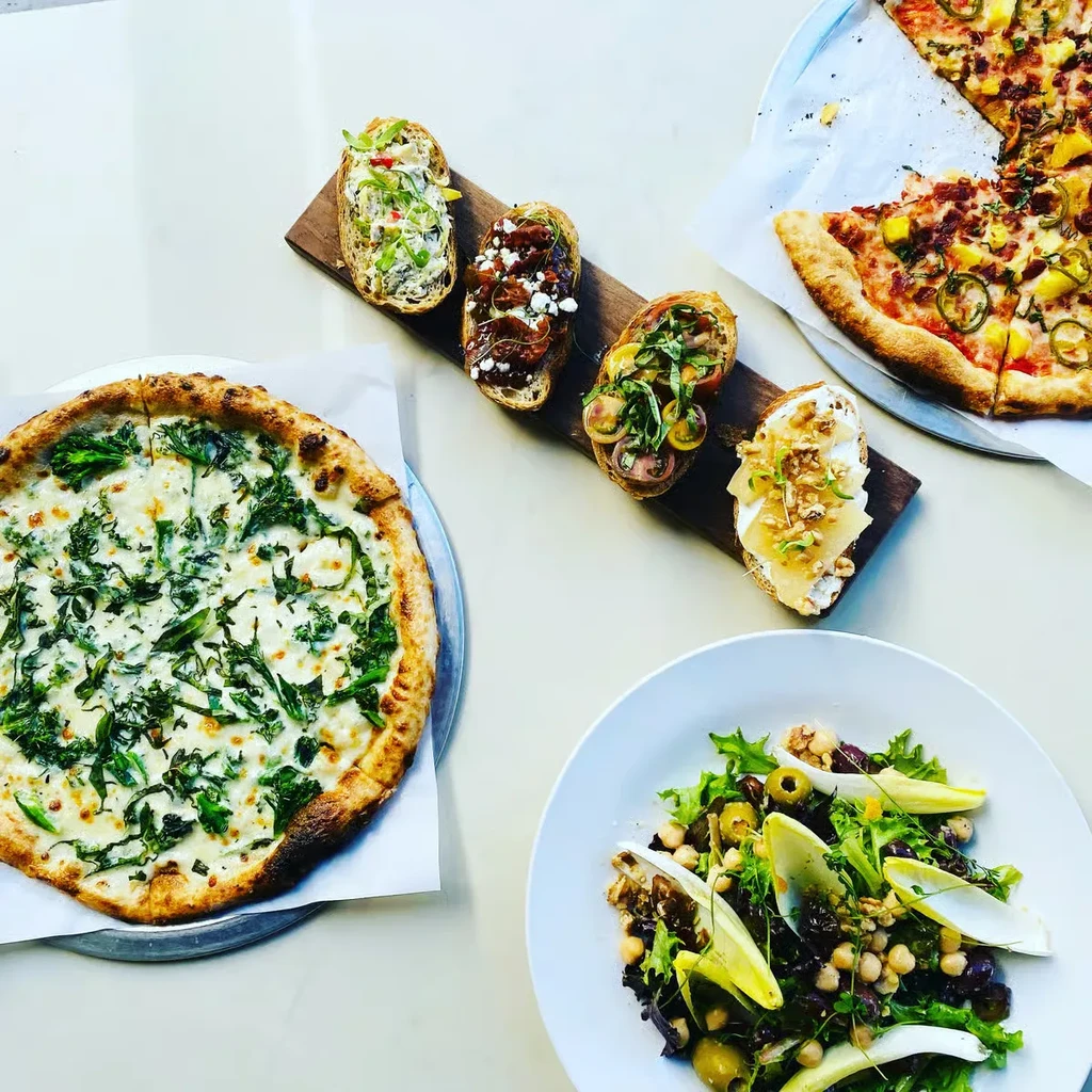 Overhead view of two pizzas, bruschetta, and a colorful salad.