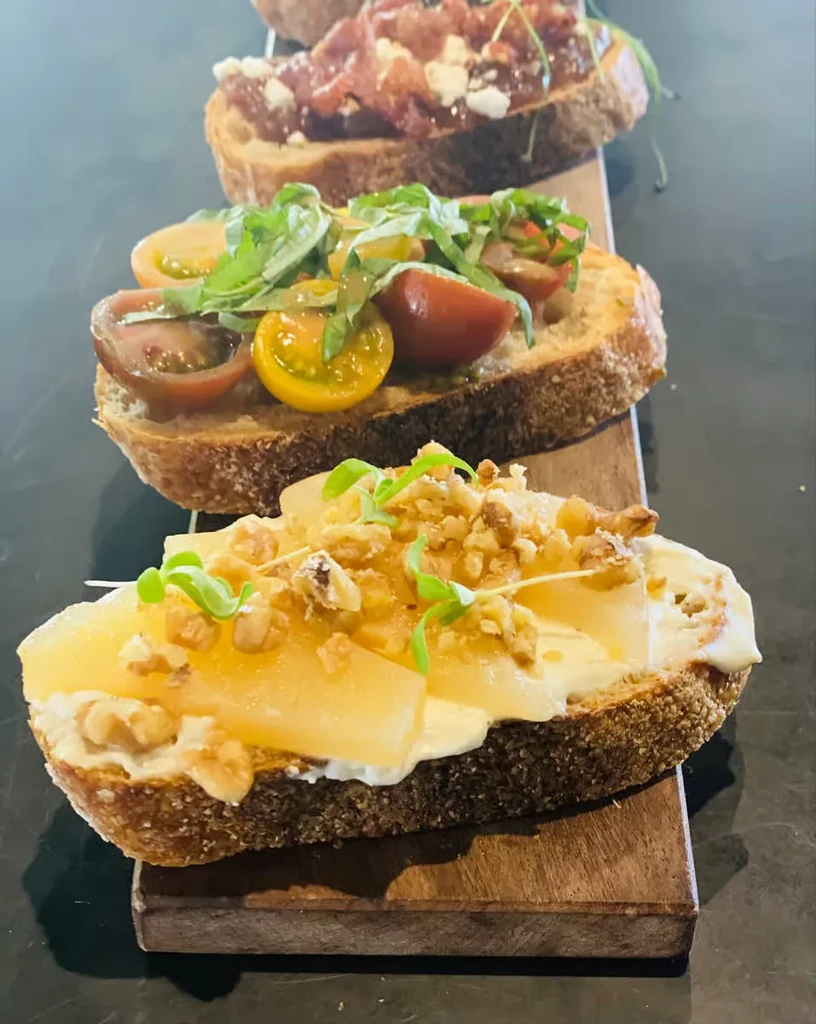 Trio of bruschetta with fruit, tomato, and meat on wooden board.