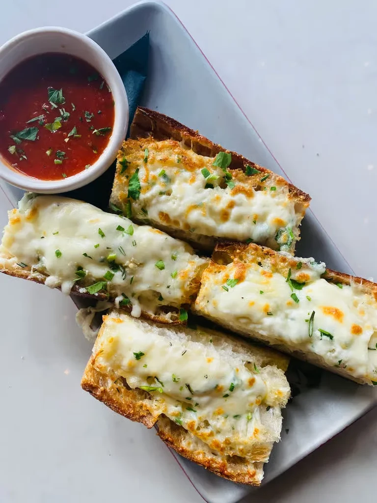 Golden brown cheesy garlic bread with herbs and marinara dip.