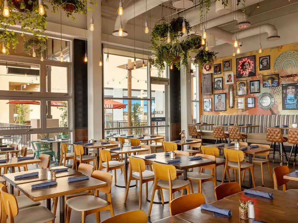 Stylish empty restaurant interior with high ceilings, plants, and gallery wall.
