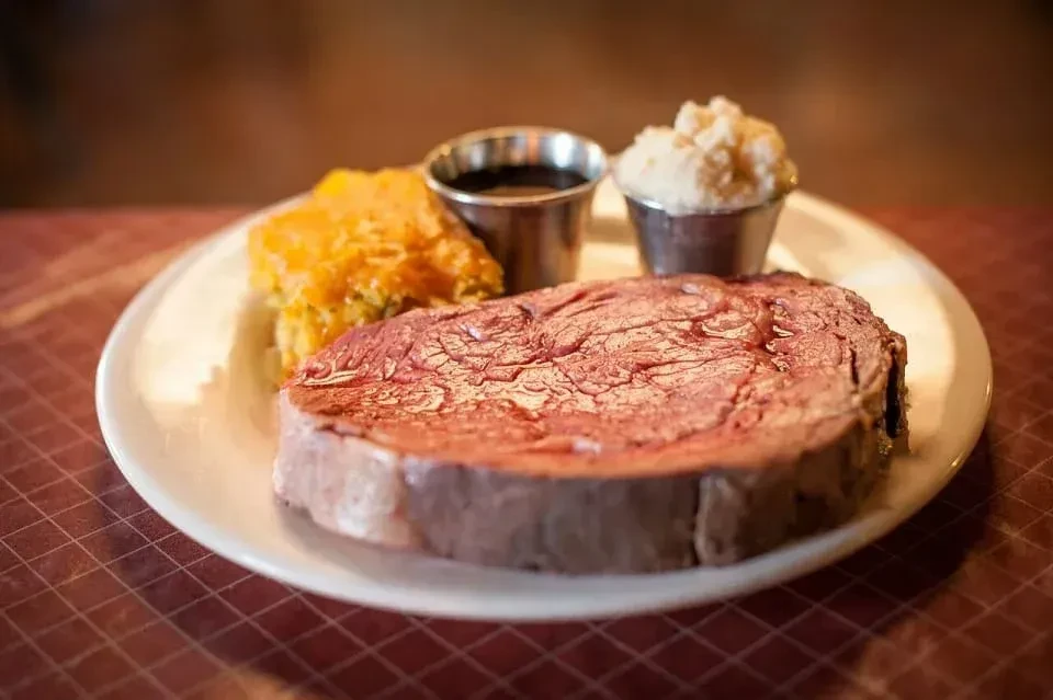 Medium-rare prime rib, mashed potatoes, au jus, and squash gratin on a plate.