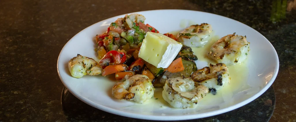 Close-up of grilled shrimp, colorful vegetables, and brie-like cheese.