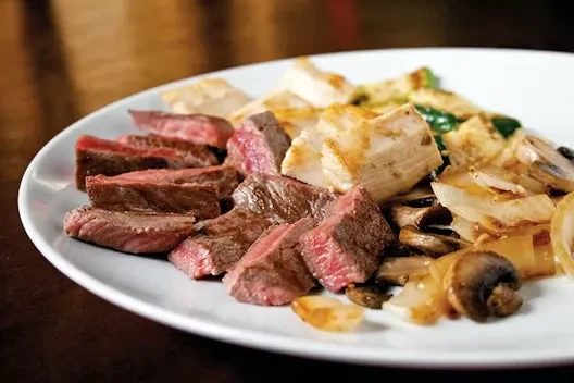 Artfully arranged meal on a white plate: steak, cubed protein, sautéed vegetables.
