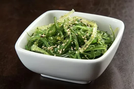 Vibrant green seaweed salad in a white bowl with sesame seeds.