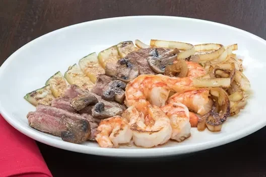 Plate of cooked shrimp, medium-rare steak, and mixed vegetables.