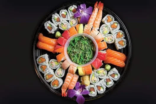 Circular sushi platter with sushi, sashimi, shrimp, seaweed salad, and orchid garnish.