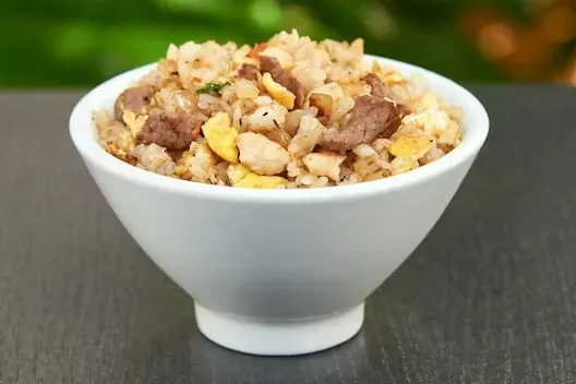 White bowl of fried rice with egg, meat, and green vegetables.