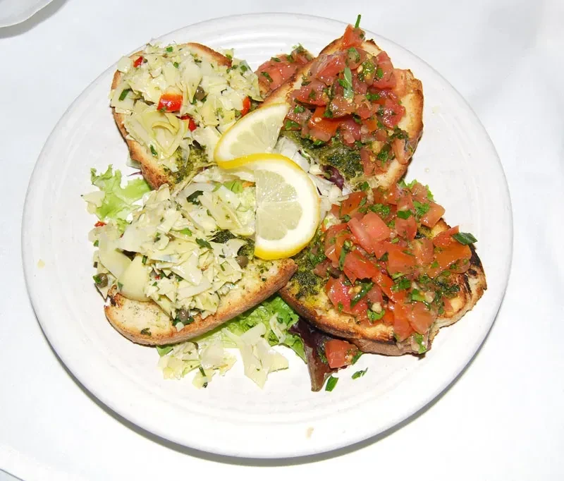 Four toasted bruschetta with tomato, artichoke, and lemon on a white plate.