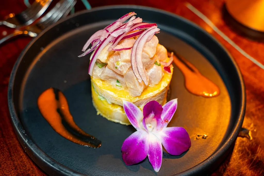 Artfully plated seafood causa stack, garnished with red onions and orchid.