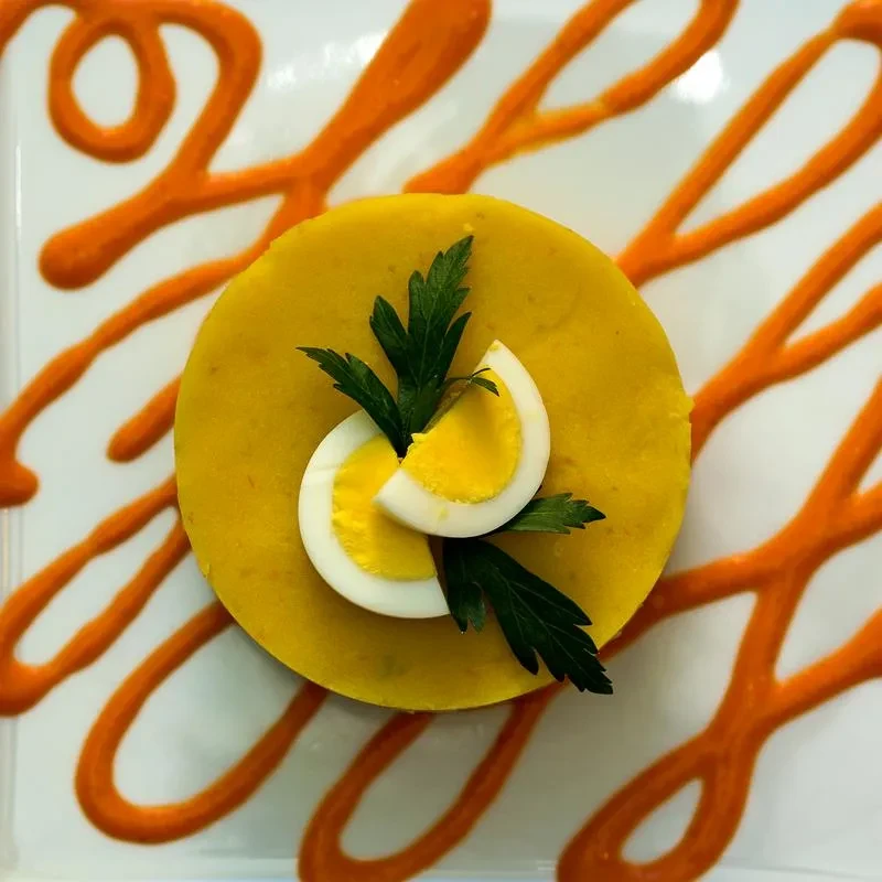 Circular yellow food, egg, parsley, and swirling orange sauce on plate.