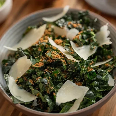 Close-up of a bowl of kale salad with Parmesan and toasted topping.