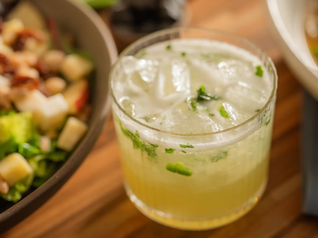 Pale green drink with ice, mint, and foam on a wooden table.