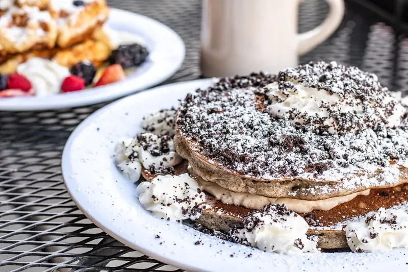 Pancakes with crushed cookies, whipped cream; waffle with berries in background.
