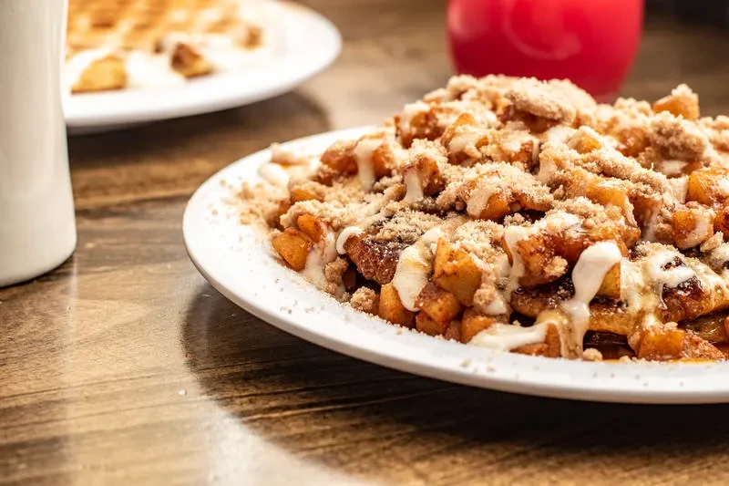 Diced golden-brown dessert with streusel and white glaze on a white plate.