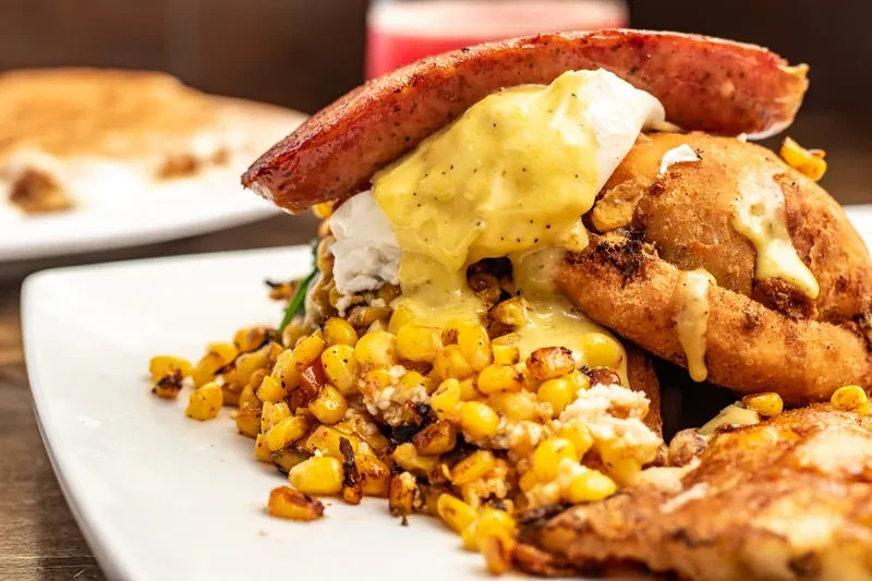 Stacked sausage, poached egg, hollandaise, and corn kernels on a plate.
