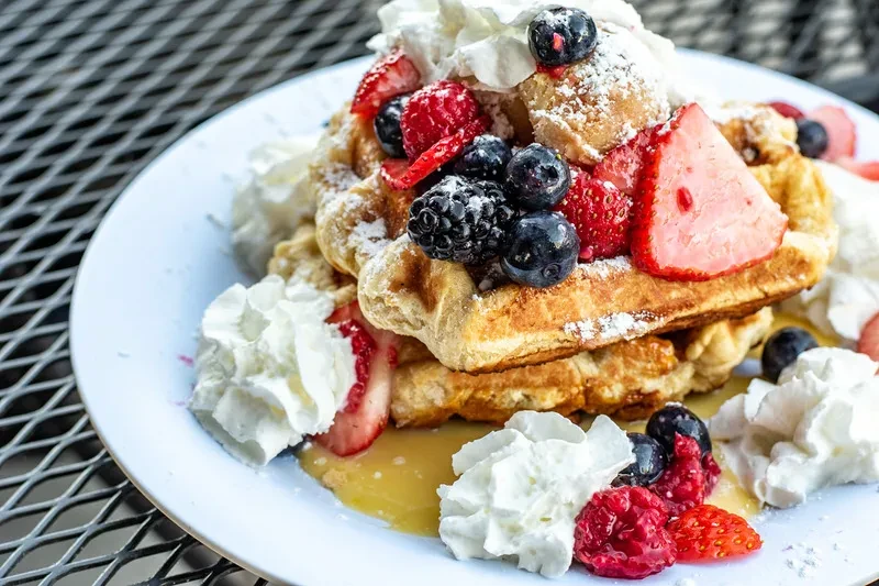 Waffles with fresh berries, whipped cream, syrup on an outdoor table.