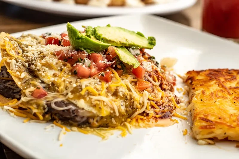 Green chilaquiles or enchiladas with avocado, pico de gallo, cheese, and hashbrown.