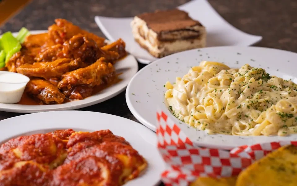Spread of Italian-American dishes: wings, marinara pasta, fettuccine alfredo, tiramisu.