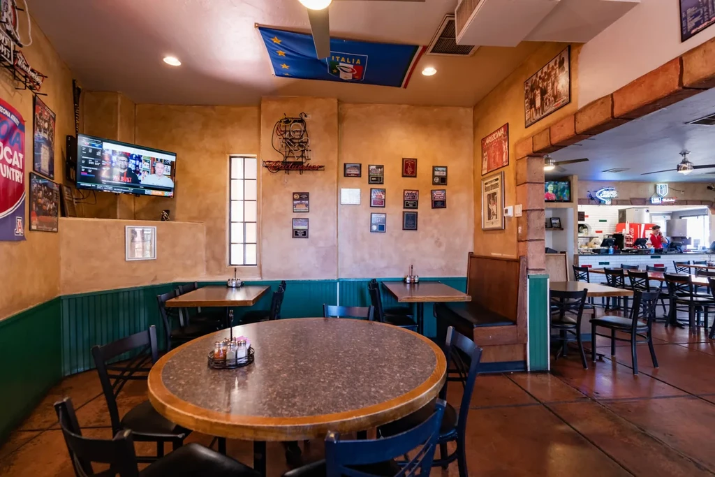 Warm pizzeria dining room featuring tables, sports memorabilia, and a TV.