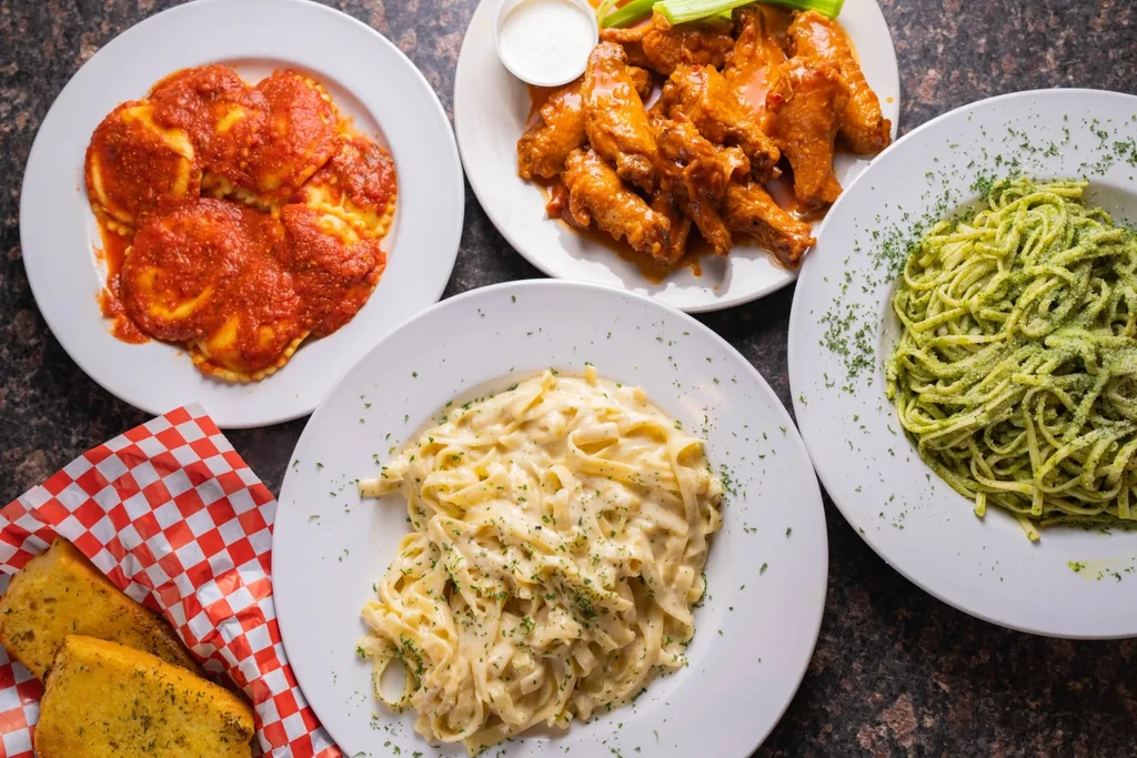 Top-down view of ravioli, wings, fettuccine, pesto pasta, and garlic bread.