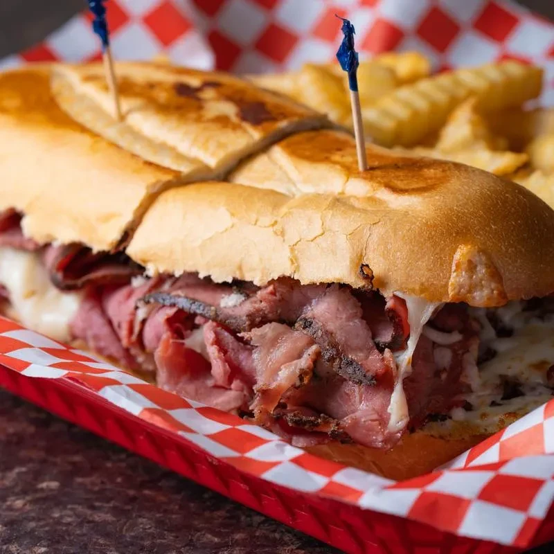 Sub sandwich with sliced red meat, melted cheese, and crinkle fries.