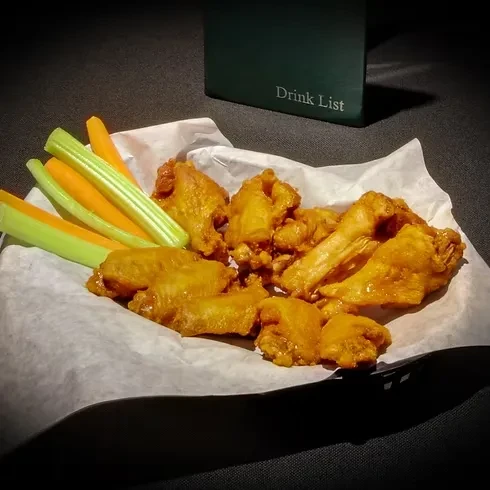 Sauced chicken wings in a basket with celery and carrot sticks.
