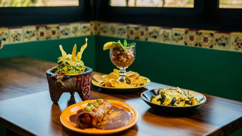 Guacamole, ceviche, and a sauced burrito on a wooden table in a restaurant.