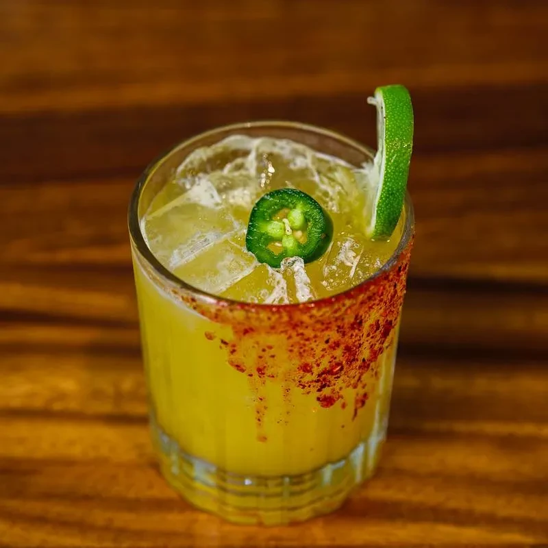 Yellow-green cocktail with ice, jalapeño, lime, and a spiced rim.