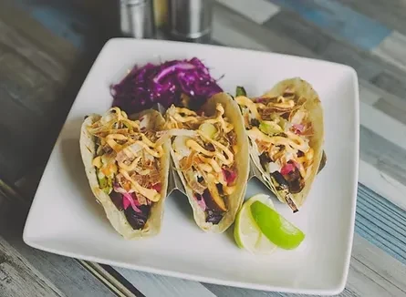 Three pulled meat tacos with sauce, red onion, lime, and cabbage.