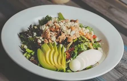 Gourmet salad with chicken, greens, cheese, avocado, and egg on wood.
