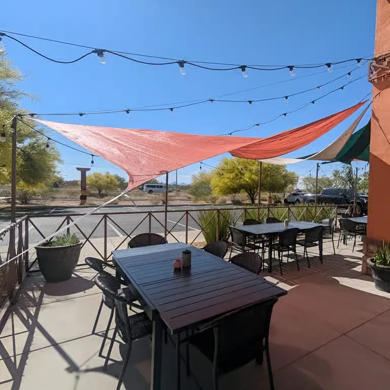 Sunny outdoor restaurant patio with tables, chairs, and shade sails.