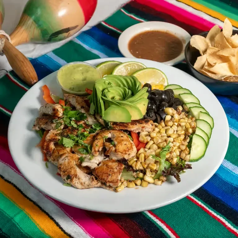 Mexican chicken salad bowl with avocado, chips, and maracas on a serape.