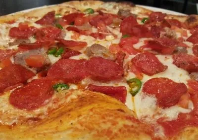 Close-up of a supreme pizza with pepperoni, sausage, tomatoes, and jalapeños.