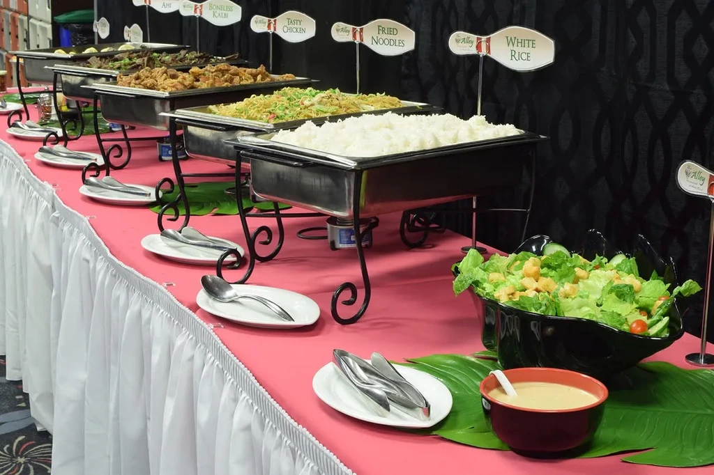 Buffet line with labeled chafing dishes, green salad, and pink tablecloth.