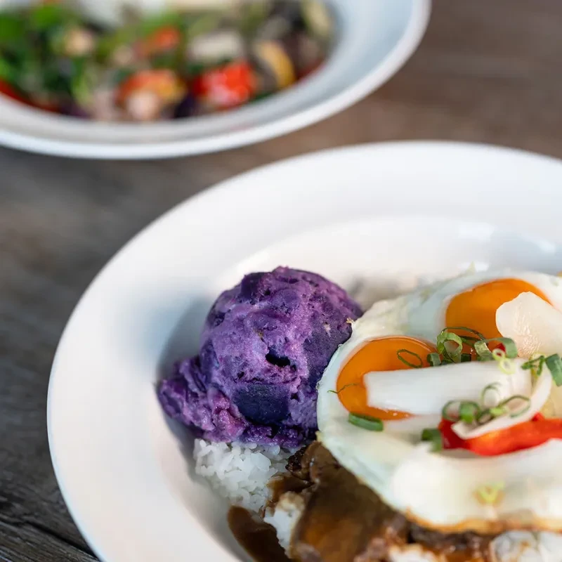Colorful dish with rice, savory base, fried eggs, and purple vegetable.