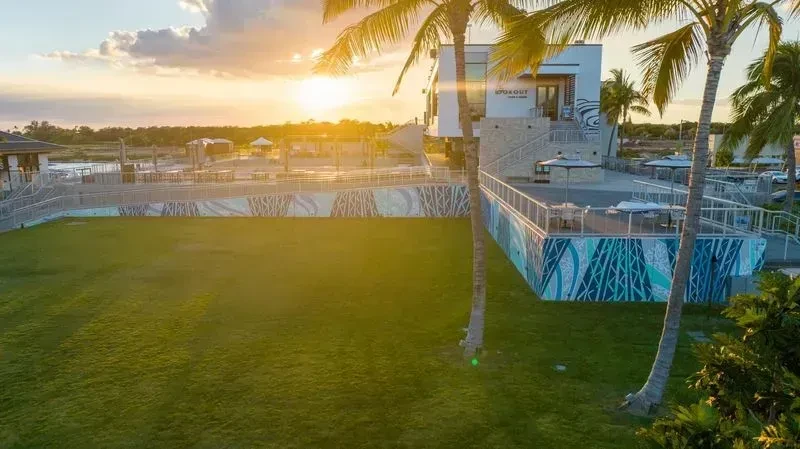 Golden hour scene of "LOOKOUT" building, lawn, palm trees, and water.