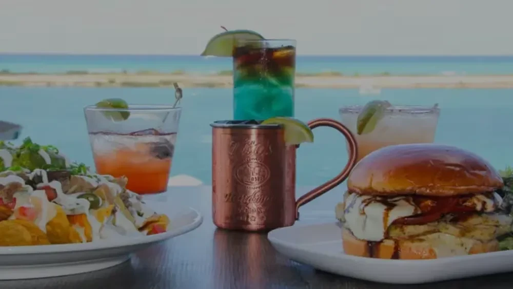 Outdoor dining: nachos, burger, and cocktails by a turquoise ocean.