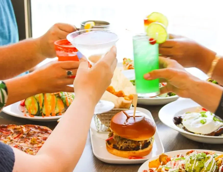 Hands toasting cocktails above a table laden with various food dishes.