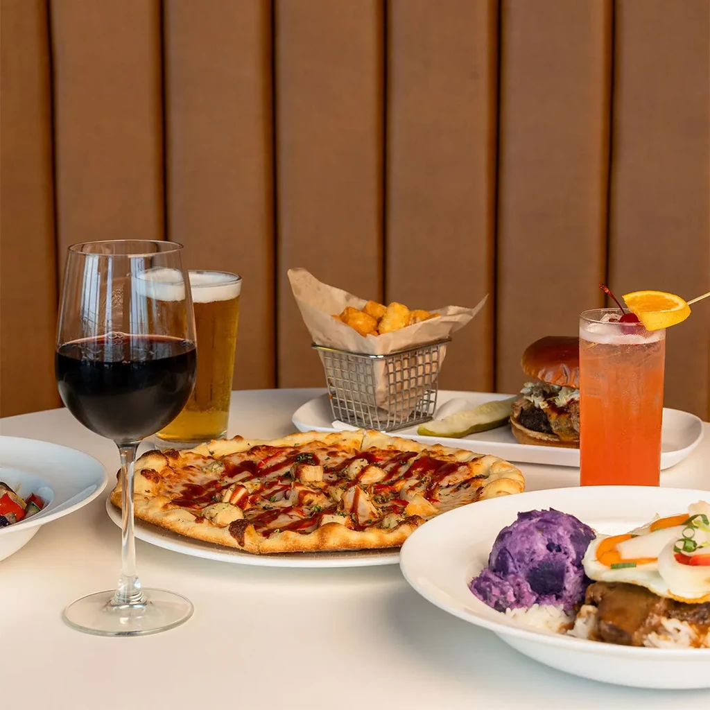 Well-arranged table with pizza, burger, Hawaiian dish, tater tots, and drinks.