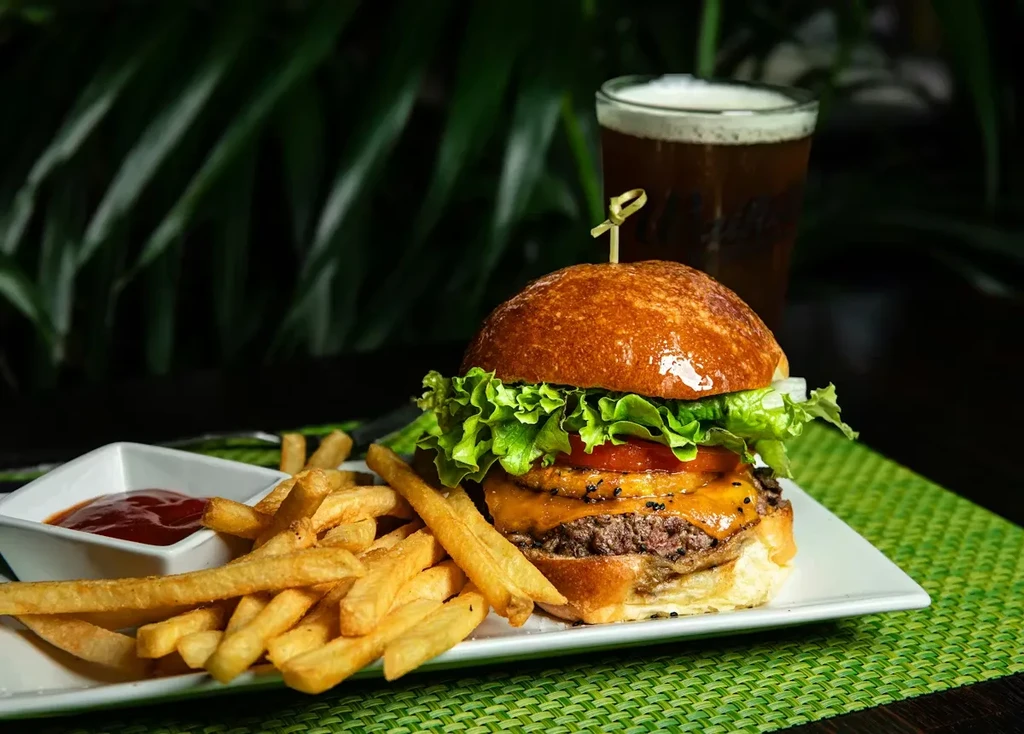 Gourmet burger, golden fries, ketchup, and beer on a green placemat.
