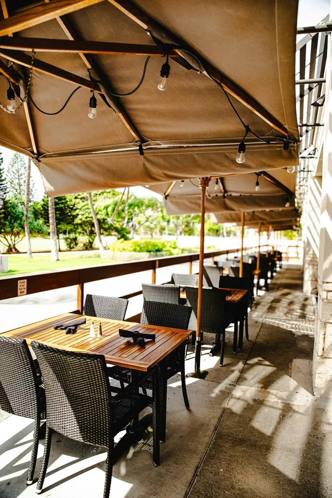 Outdoor restaurant patio with empty tables, umbrellas, and lush greenery.